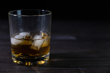 Photo of whiskey in a glass with ice. Real ice and a pleasant color of the drink on a black background.