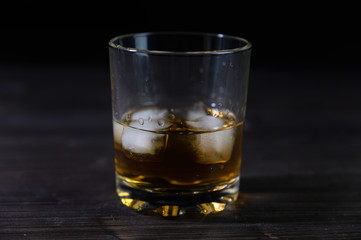 Photo of whiskey in a glass with ice. Real ice and a pleasant color of the drink on a black background.