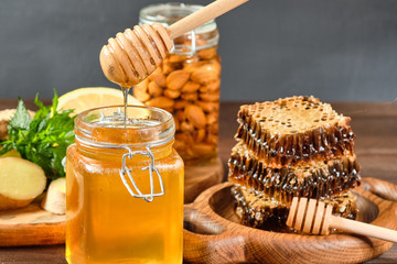 honey in honeycombs on a wooden plate and golden honey in a jar with nuts and comb for honey with lemon and ginger