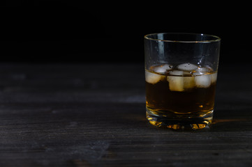 Photo of whiskey in a glass with ice. Real ice and a pleasant color of the drink on a black background.