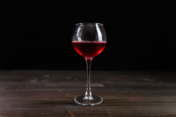 Photo of red wine in a glass on a wooden table. Nice color drink on a black background.
