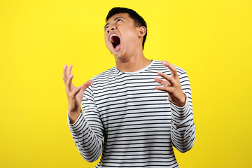 Young funny Asian man doing angry gesture, annoyed, and emotional, isolated on yellow