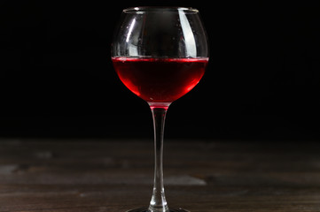Photo of red wine in a glass on a wooden table. Nice color drink on a black background.
