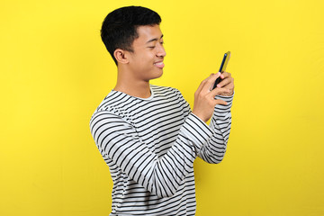 Happy young good looking Asian man smiling using smartphone