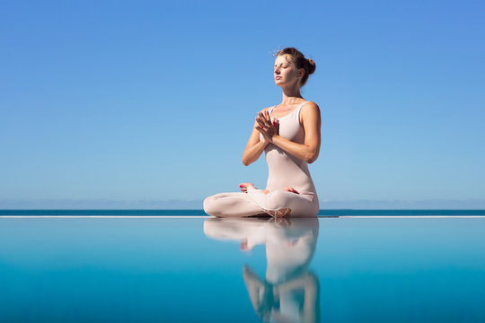 Side view of a beautiful young slender woman sitting in lotus position and meditating on the edge of the pool on a blue sky. Concept of yoga relaxation and meditation. Copyspace