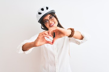 Beautiful businesswoman wearing glasses and bike helmet over isolated white background smiling in love doing heart symbol shape with hands. Romantic concept.