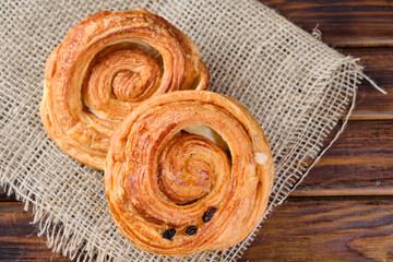 puff buns with jam and raisins in the shape of a snail on burlap and wooden background. Selective focus