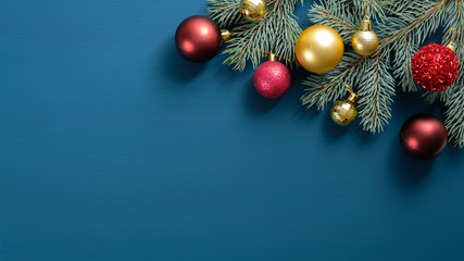 Christmas tree branch with red and golden balls on blue background. Flat lay, top view. Xmas greeting card mockup with copy space.