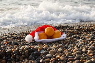 Obraz premium Santa Claus hat with tangerines on the beach
