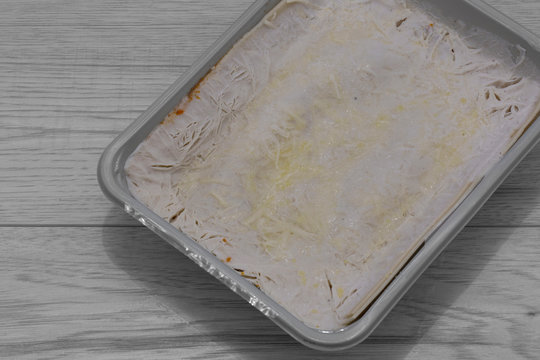 Frozen beef lasagne, or lasagna, in a plastic tray packaging. Frozen ready meal on a grey wood background