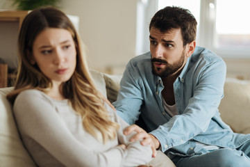 Young man asking his girlfriend for forgiveness at home