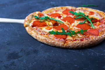 A fresh prepared pepperoni pizza with salami, tomatoes and cheese on a dark background. Italian...