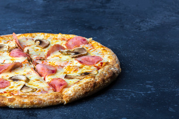 A fresh prepared pizza with with mushrooms, ham and cheese on a dark background. Italian traditional lunch or dinner. Fast food and street food concept. Flat ly, top view, copy space fot text