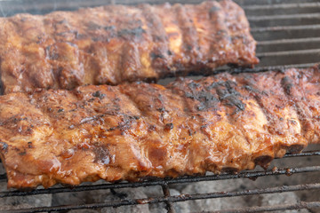 A close up view of beef spare ribs cooking on a open braai or barbecue on a warm summers day