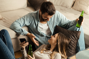 Young couple enjoying in MP3 music while drinking beer at home