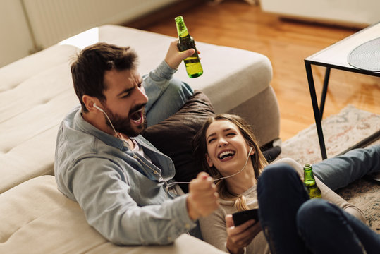 Young couple enjoying in MP3 music while drinking beer at home