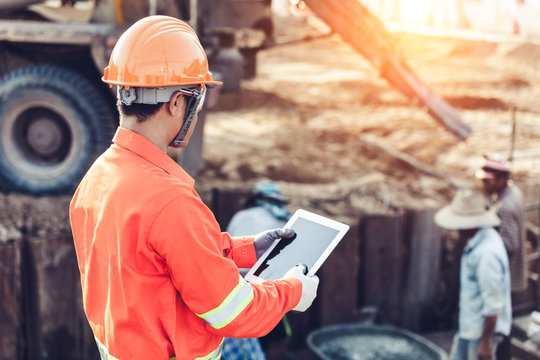Asian engineer with hardhat using tablet inspecting and working at construction site