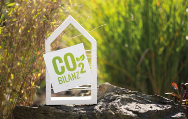 Weißes Haus im Garten mit Schild CO2 Bilanz