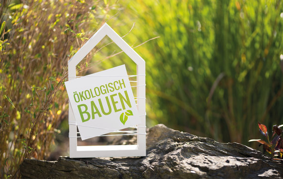 Wei&szlig;es Haus im Garten mit Schild &Ouml;kologisch Bauen