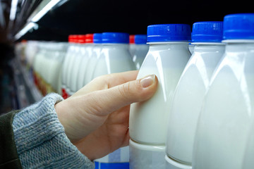 Womans hand holding milk bottle in supermarket. Man shopping milk in grocery store. Close-up.