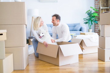 Fototapeta premium Young beautiful couple with dog sitting on the floor at new home around cardboard boxes