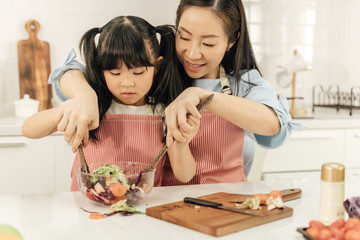 Young asian family cooking food in kitchen.Cute little girl and her beautiful parents are making salad and smiling while cooking in kitchen at home.Happy family in the kitchen concept.