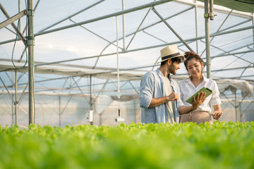 Smart farm,sensor technology,smart agriculture concept.Farmer and partner with tablet for working organic hydroponic vegetable garden at greenhouse in morning.copy space.