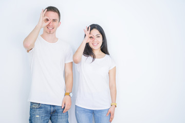 Young beautiful couple wearing casual t-shirt standing over isolated white background doing ok gesture with hand smiling, eye looking through fingers with happy face.