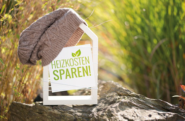 Weißes Haus im Garten mit Schild Heizkosten sparen