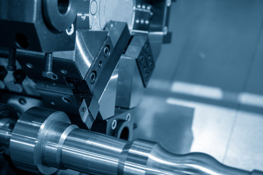 The operation of multi-tasking CNC lathe machine cutting the metal shaft parts in the light blue scene. The hi-technology mechanical parts manufacturing process by CNC turning machine.