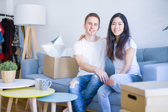 Young beautiful couple sitting on the sofa drinking coffee at new home around cardboard boxes