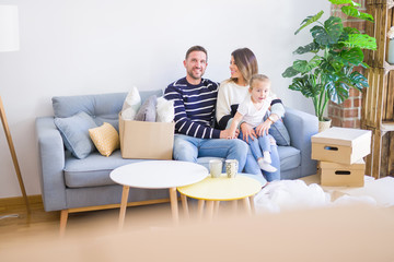 Beautiful family with kid sitting on the sofa drinking coffee at new home around cardboard boxes