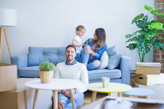 Beautiful family, parents sitting on the sofa looking his kid jumping at new home around cardboard boxes
