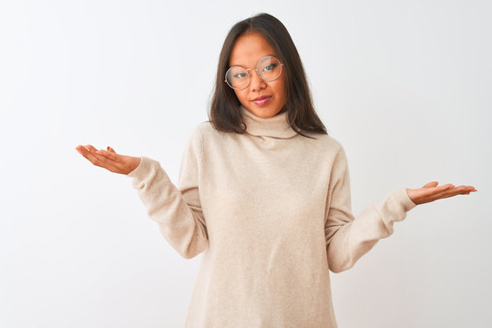 Young chinese woman wearing turtleneck sweater and glasses over isolated white background clueless and confused expression with arms and hands raised. Doubt concept.