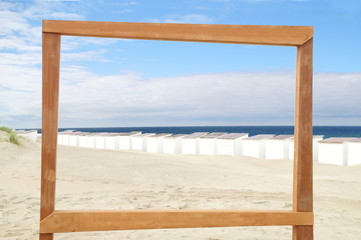 Empty wooden picture frame on the beach sand. Little white beach cabins, beach and sea background with frame design for creative advertising Summer vacation and travel concept. Copy space