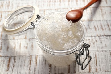 dead sea salt in glass jar with bamboo spoon on rustic white wood background closeup