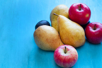 Fresh organic pears, apples, plums on a blue wooden background. Autumn harvest. Free space for text.