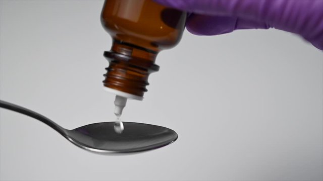 Close up of hand in medical glove dropping liquid with a dropper bottle on a teaspoon