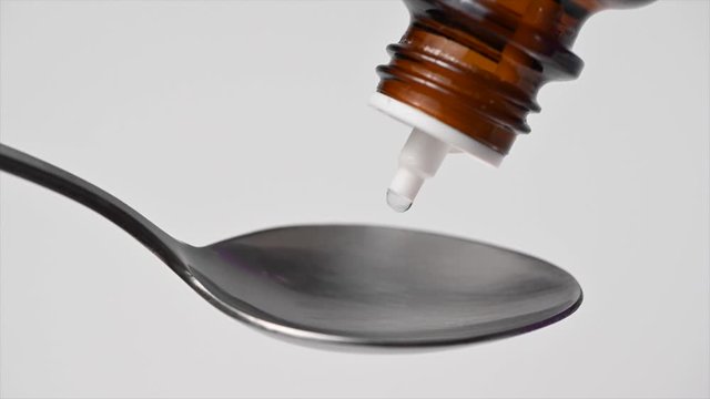 Close up of hand in medical glove dropping liquid with a dropper bottle on a teaspoon