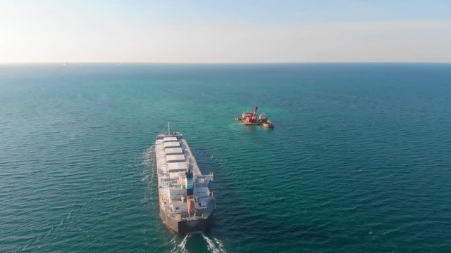 The large cargo vessel left the port after loading and moves in the right direction at high speed. Balker goes in the ocean.