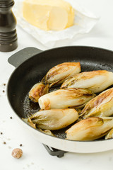 Braised chicory on the belgian way in a baking pan with butter and pepper grinder