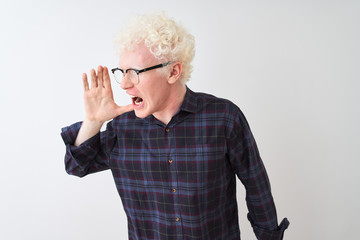 Young albino blond man wearing casual shirt and glasses over isolated white background shouting and screaming loud to side with hand on mouth. Communication concept.