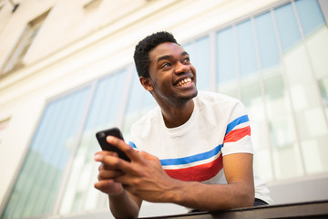 happy young black man with mobile phone outside in city