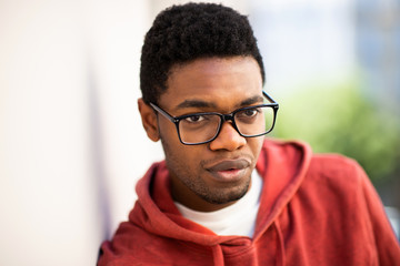 Obraz premium Close up of young african american man with eyeglasses and serious expression leaning against wall