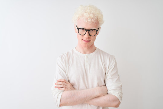 Young albino blond man wearing t-shirt and glasses standing over isolated white background skeptic and nervous, disapproving expression on face with crossed arms. Negative person.
