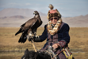 Portrait of a traditional kazakh eagle hunter with his golden eagle on horseback. Ulgii, Mongolia. - obrazy, fototapety, plakaty