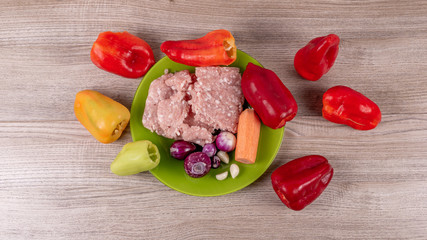 Ingredients for stuffing peppers, minced pork, onions, garlic, carrots laid out on a green plate and peeled peppers laid out on a plate