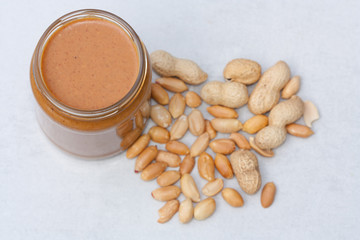 Creamy peanut butter in jar and peanuts.