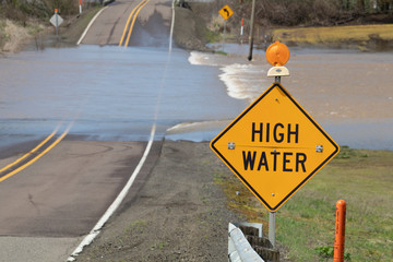 High water warning sign with floodwater crossing the road near Albany, Oregon.