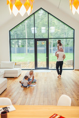 White interior of room, big panoramic windows. Family playing with each other. Cheerful parents and children at home